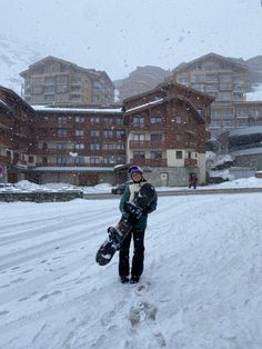 a man holding a snowboard standing in the middle of a snowy road with buildings behind him