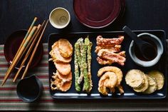 an assortment of sushi on a black plate with chopsticks next to it