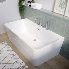 a white bath tub sitting on top of a wooden floor next to a green tiled wall