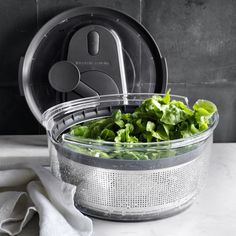 lettuce in a strainer with a lid on a counter top next to a white towel