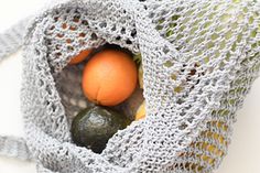 two oranges and an avocado are in a crocheted gray bag