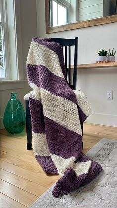 a purple and white striped blanket sitting on top of a wooden floor next to a chair