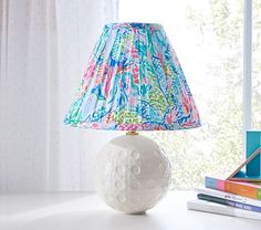 a lamp on a white table next to books and a window with curtains in the background