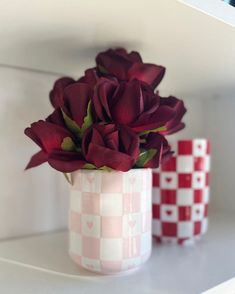 two vases with flowers in them sitting on a shelf next to red and white checkered cups