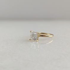 a yellow gold engagement ring with a princess cut diamond in the center on a white surface