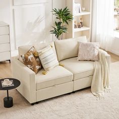 a living room with a white couch and some pillows on the floor next to a coffee table