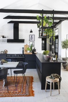 a kitchen with black and white walls, an oven, counter tops, chairs and plants hanging from the ceiling