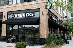 people sitting at tables in front of starbucks's on the corner of a street