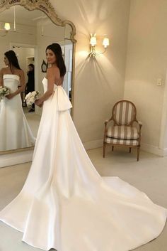 a woman standing in front of a mirror wearing a wedding dress with bow at the waist