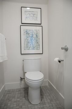 a white toilet sitting in a bathroom next to a towel dispenser and pictures on the wall