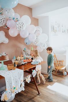 two children are standing in front of a table with balloons and cake on it,