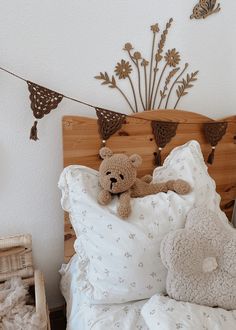 a teddy bear laying on top of a bed with white sheets and pillows in front of a wooden headboard