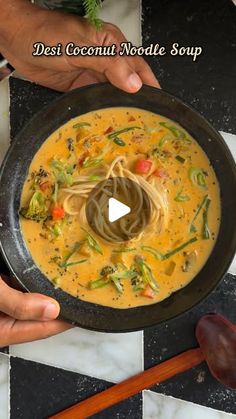 two hands holding a bowl of soup with noodles and broccoli on the side