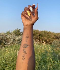 a person with a yellow marker on their left hand and tattoos on her right arm