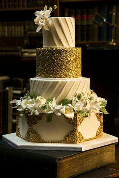 a three tiered wedding cake with gold and white flowers on top is sitting on a book