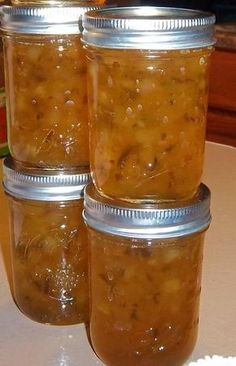 three jars filled with pickles sitting on top of a white tablecloth covered counter