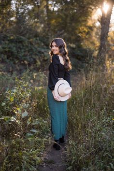 a woman standing in tall grass with a hat on her head and looking off into the distance