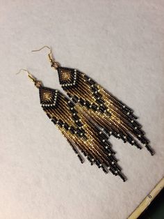 black and gold beaded fringe earrings on white paper next to pen with clipping