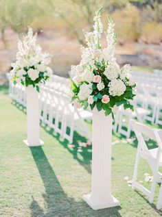 two tall white vases with flowers on them are sitting in front of rows of chairs