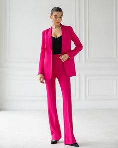 a woman in a bright pink suit and black top is standing with her hands on her hips