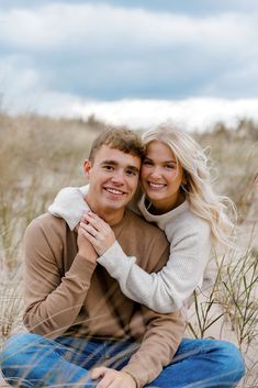 a man and woman are sitting in the sand with their arms wrapped around each other