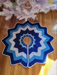 a blue and white crocheted blanket sitting on top of a wooden floor next to a christmas tree