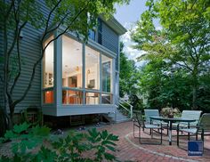 a patio with tables and chairs in front of a house that is surrounded by trees