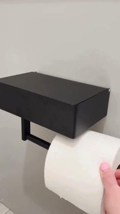 a person holding a roll of toilet paper in front of a black wall mounted shelf