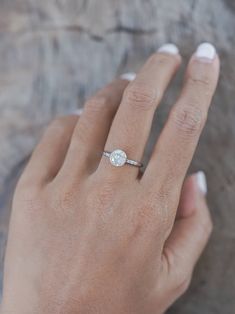 a woman's hand with a diamond ring on top of her left hand, against a rock surface