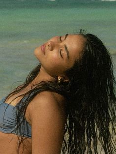 a woman laying on the beach with her eyes closed and hair blowing in the wind