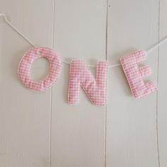 a pink and white gingham banner with the word one hanging from it's string