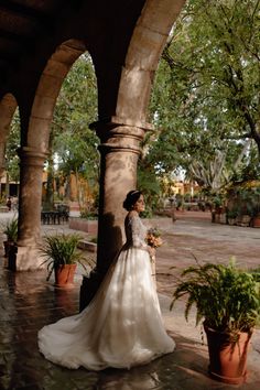 a woman in a wedding dress is standing under an archway with potted plants on either side