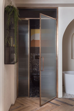 a bathroom with a glass shower door next to a bathtub and plant on the wall