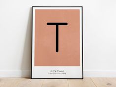 a poster with the letter t on it in black and tan frame against a white wall