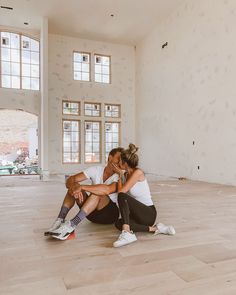 two people sitting on the floor in an empty room, one is kissing the other