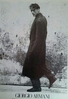 a black and white photo of a man in a long coat walking down the street