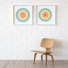 two paintings hang on the wall next to a wooden chair in front of a white brick wall