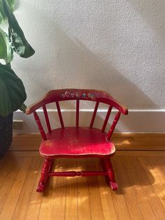 a red wooden chair sitting on top of a hard wood floor next to a potted plant