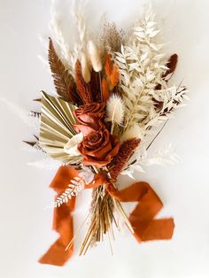 an arrangement of dried flowers and foliage on a white surface with red ribbon tied around it