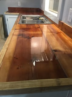 a kitchen counter made out of wood with a sink and window in the back ground