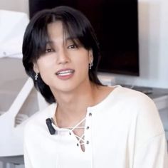 a woman with black hair wearing a white shirt and silver earring, standing in front of a piano