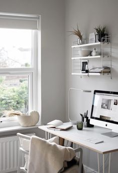 a white desk with a computer monitor and keyboard sitting on top of it next to a window