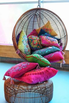 a wicker hanging chair filled with colorful pillows