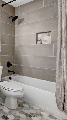 a white toilet sitting in a bathroom next to a bath tub and shower head mounted on the wall