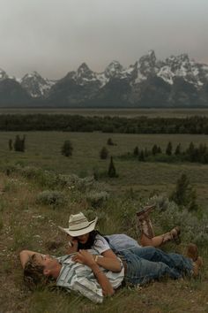 two people laying on the ground in a field with mountains in the backgroud