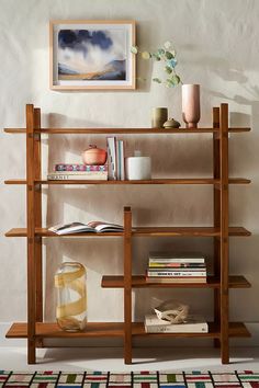 a wooden shelf with books and vases on it in front of a white wall