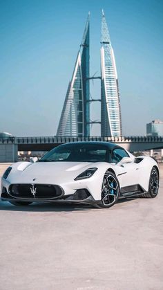 a white sports car parked in front of a tall building with a sky scraper behind it