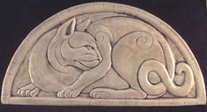 an animal carved into the side of a stone wall plaque with two cats on it