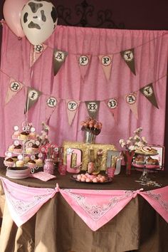 a table topped with cake and desserts next to a cow theme wall hanging from the ceiling