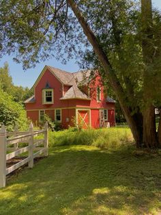 a red house with a white fence in front of it and trees around the yard